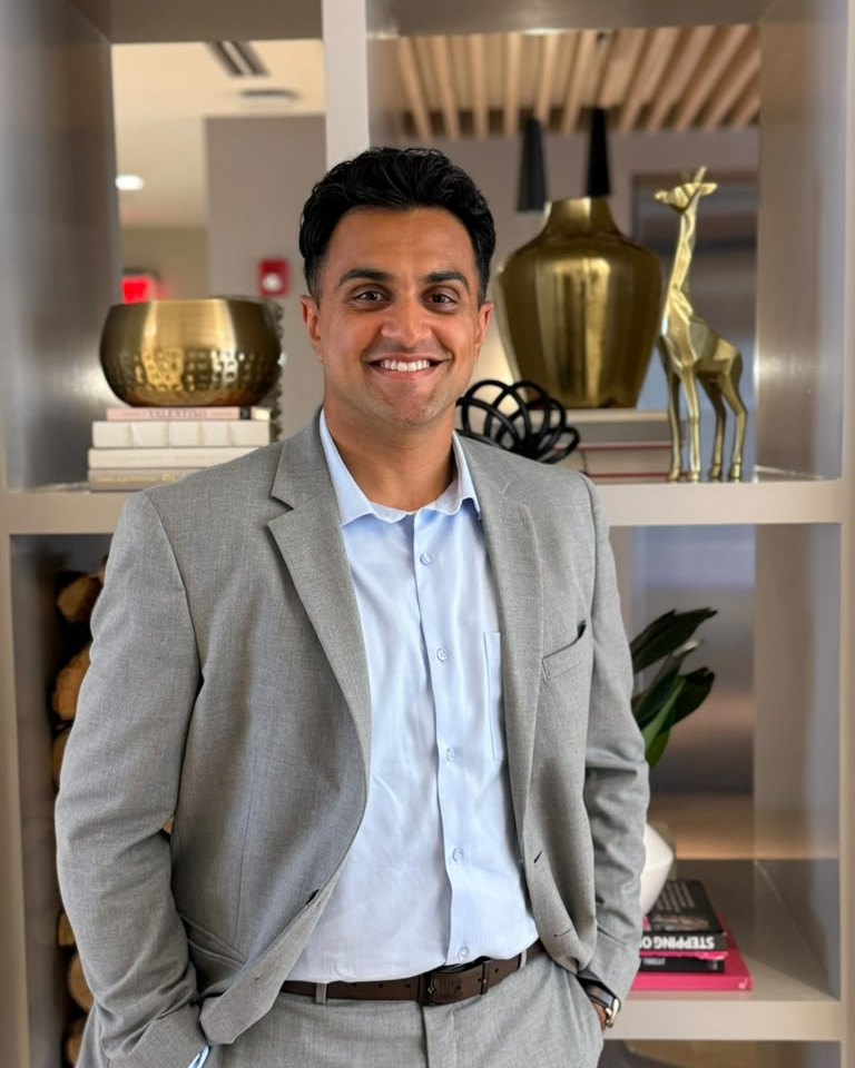 Kiran Aiyar standing near a shelf of books.